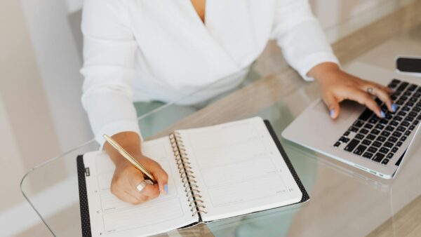 Persona che scrive appunti su un quaderno mentre lavora al laptop